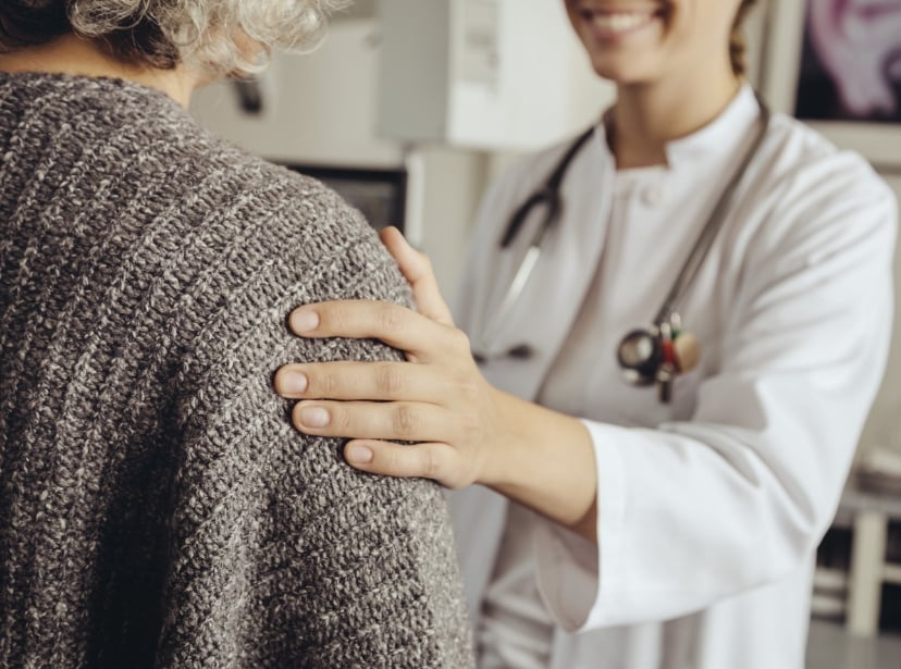 Läkare håller en hand på en patients axel.